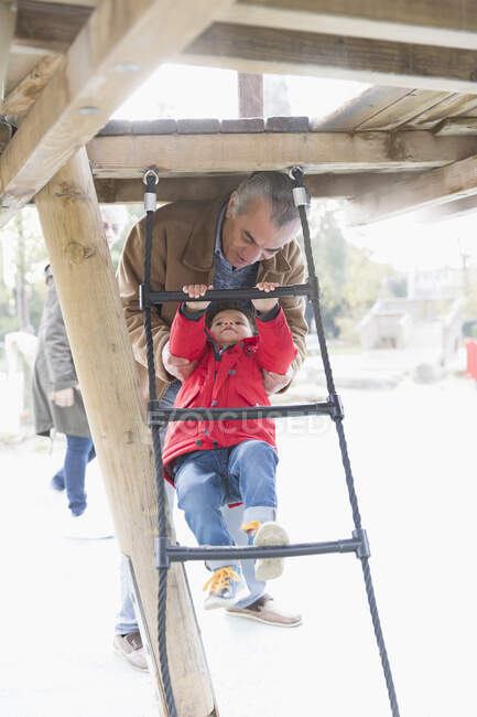 Grand-père jouant avec petit-fils sur l'échelle de terrain de jeu — Photo de stock