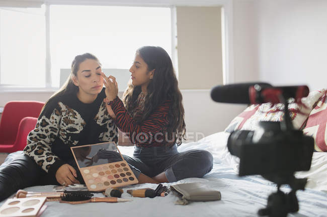 Adolescentes niñas vlogging acerca de la aplicación de maquillaje en la cama en el dormitorio - foto de stock