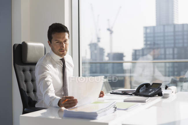 Geschäftsmann liest Papierkram in sonnigem, städtischem Büro — Stockfoto