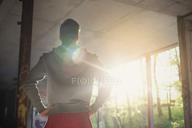 Молодий чоловік бігун відпочиває, стоячи руками на стегнах у сонячно покинутій будівлі — стокове фото