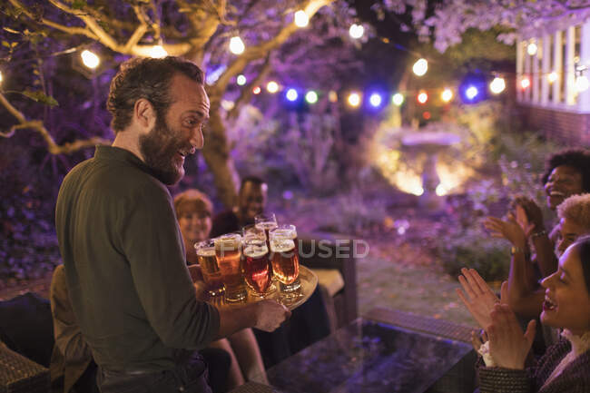 Uomo sorridente con vassoio di birre che servono amici alla festa in giardino — Foto stock