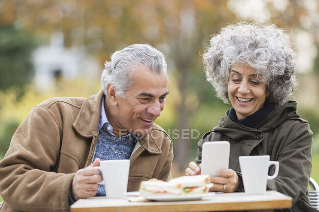 Casal de idosos com telefone inteligente, almoçando e bebendo café no parque — Fotografia de Stock