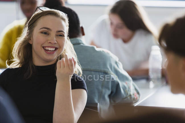Счастливая, улыбающаяся школьница разговаривает с одноклассницей в классе — стоковое фото