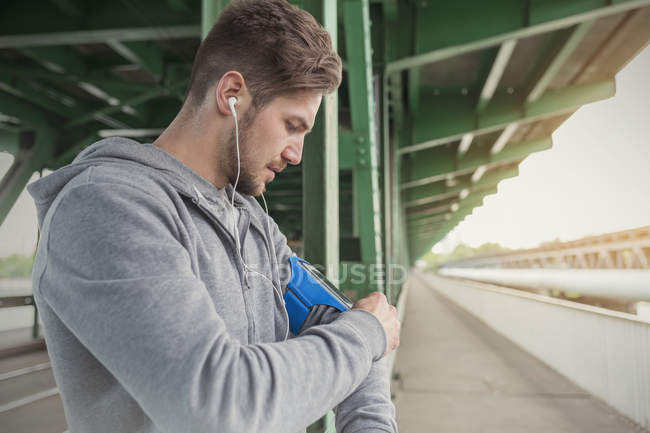 Young male runner listening to music with earphones and mp3 player arm band — Stock Photo