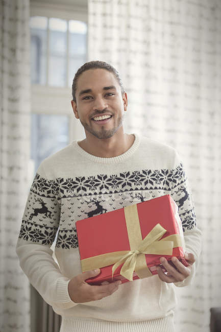 Portrait smiling young man in Christmas sweater holding gift — Stock Photo