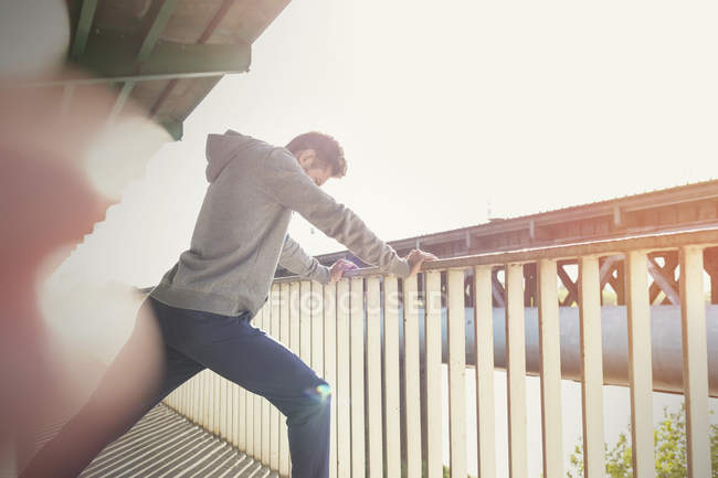 Young male runner stretching leg at sunny urban railing — Stock Photo
