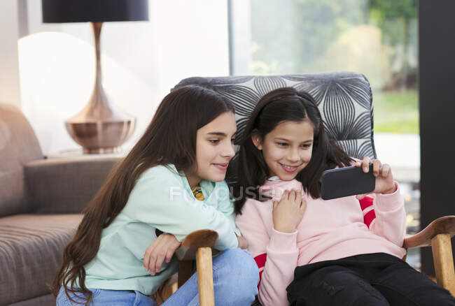 Hermanas usando teléfono inteligente en la sala de estar - foto de stock