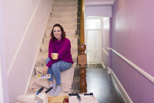 Portrait confident woman redecorating, looking at paint swatch on stairs — Stock Photo