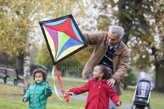 Grand-père et petits-enfants volant un cerf-volant dans le parc d'automne — Photo de stock