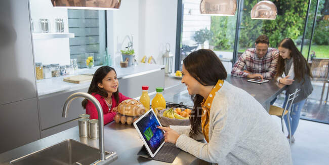 Family talking, using digital tablets in kitchen — Stock Photo