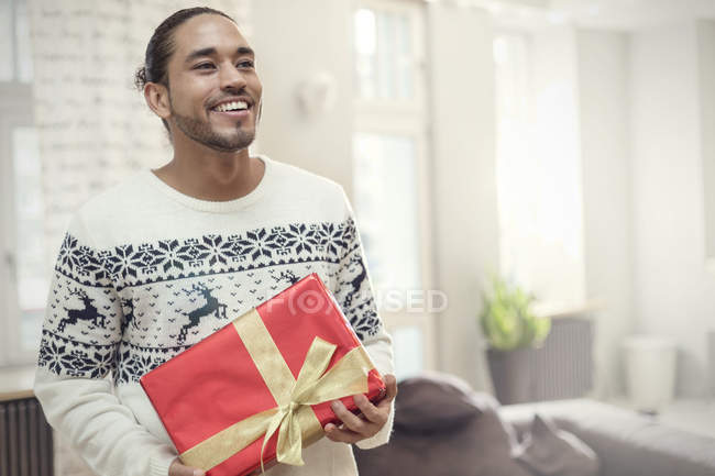 Junger Mann im Weihnachtspullover hält Geschenk in der Hand — Stockfoto