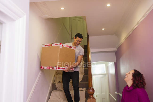 Casal feliz saindo de casa, carregando caixa de papelão escadas abaixo — Fotografia de Stock