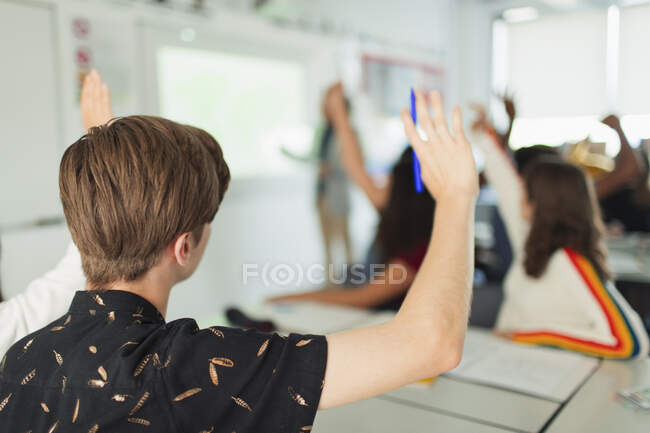 High school boy student with hand raised during lesson in classroom — Stock Photo