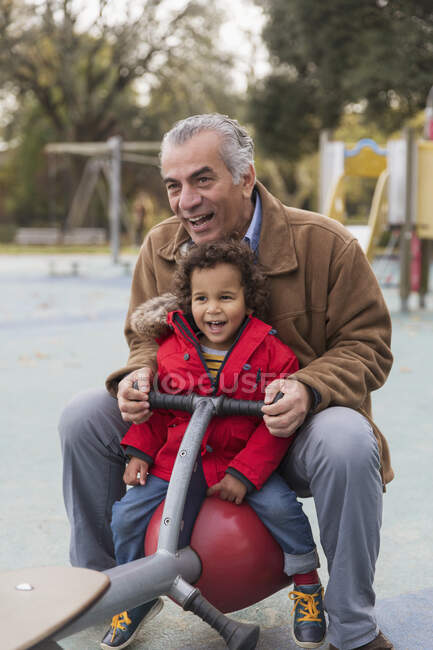 Grandfather playing with grandson on playground seesaw — Stock Photo