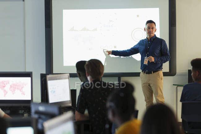 Чоловік молодший викладач провідний урок на проекційному екрані в класі — стокове фото