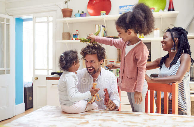Young family playing with toy dinosaurs in kitchen — Stock Photo