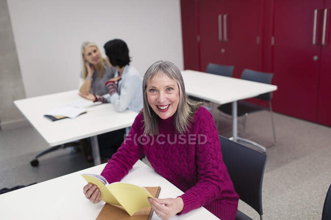 Retrato sonriente, confiada estudiante universitaria comunitaria leyendo en el aula - foto de stock