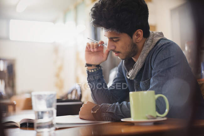 Joven estudiante universitario enfocado estudiando en la cafetería - foto de stock