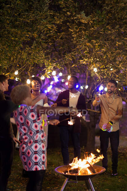 Amigos felices con bengalas alrededor de hoguera en la fiesta del jardín - foto de stock