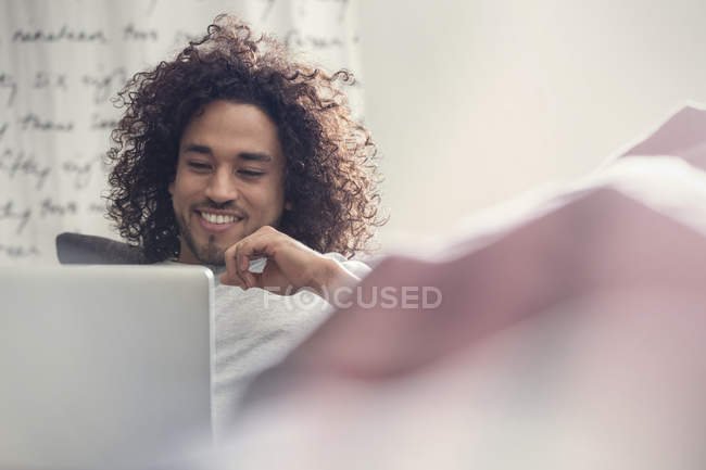Sorridente giovane uomo utilizzando il computer portatile sul divano — Foto stock