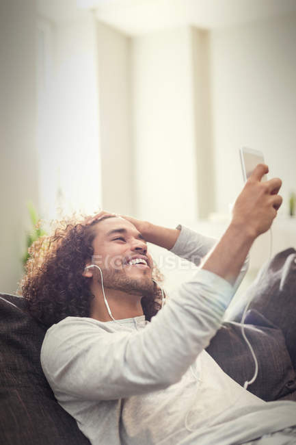 Jovem feliz ouvindo música com fones de ouvido e mp3 player no sofá — Fotografia de Stock