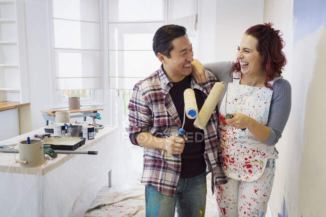 Feliz, pareja juguetona con rodillos de pintura sala de pintura - foto de stock