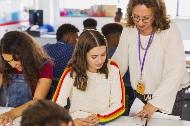 Female high school teacher helping girl student doing homework in classroom — Stock Photo