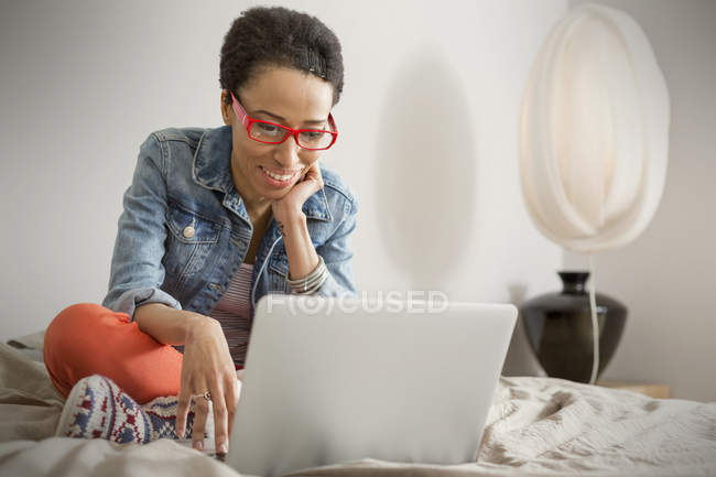 Sorridente giovane donna utilizzando il computer portatile sul letto — Foto stock