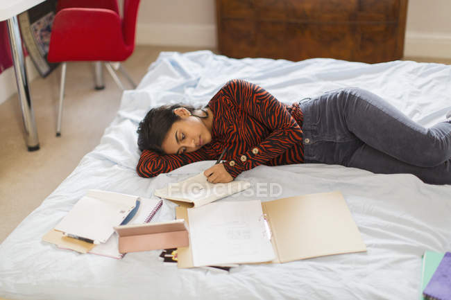 Ragazza adolescente che fa i compiti a casa sdraiato sul letto — Foto stock
