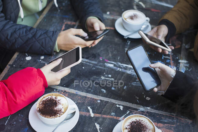 Freunde nutzen Smartphones und trinken Cappuccino am Cafétisch — Stockfoto