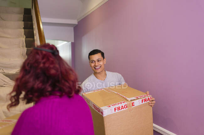 Happy couple moving into new house, carrying cardboard boxes up stairs — Stock Photo