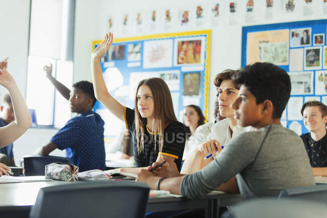 Studenti delle scuole superiori con le mani alzate, facendo domande durante la lezione in classe — Foto stock