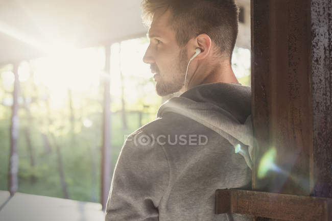 Young male runner with earphones looking over shoulder on train station platform — Stock Photo