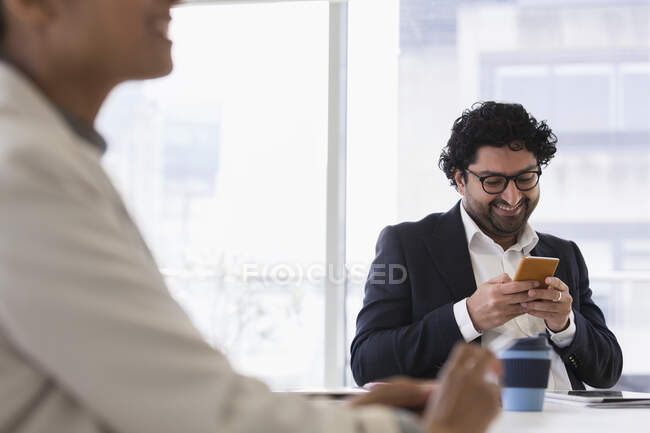 Uomo d'affari sorridente utilizzando smart phone in ufficio — Foto stock