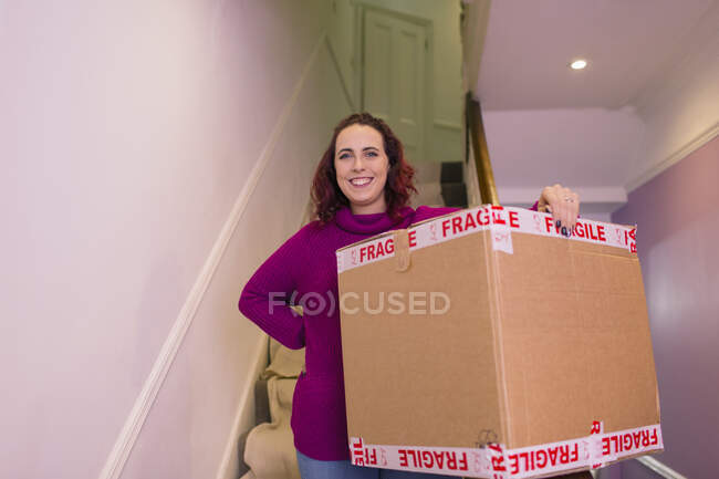 Portrait confident woman moving into new home, carrying cardboard box — Stock Photo