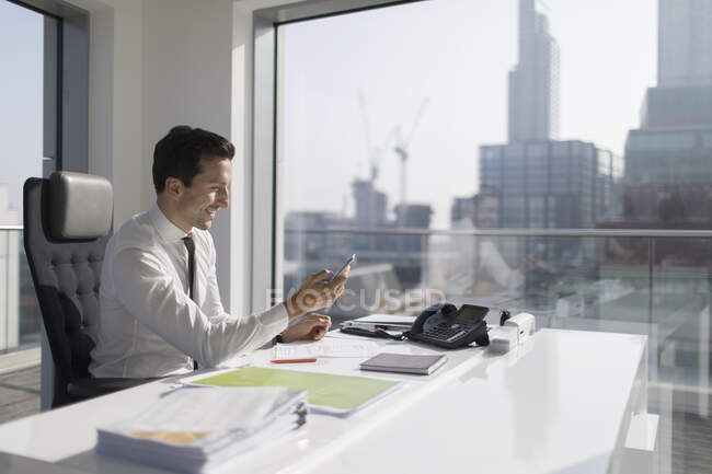 Homme d'affaires utilisant un téléphone intelligent dans un bureau ensoleillé et urbain — Photo de stock