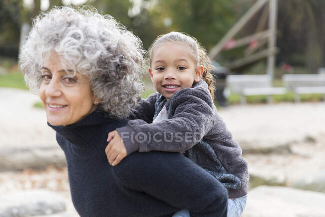 Retrato sonriente abuela piggybacking nieta - foto de stock