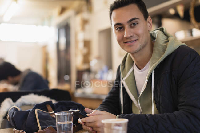 Портрет уверенный молодой студент колледжа с помощью смартфона в кафе — стоковое фото
