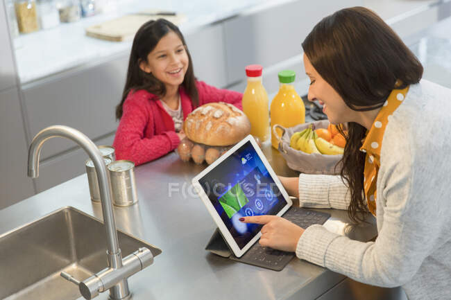 Fille regarder mère en utilisant tablette numérique dans la cuisine — Photo de stock