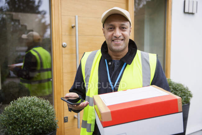 Retrato confiante, entregador amigável com pacote e telefone inteligente na porta da frente — Fotografia de Stock