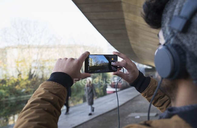 Молодой человек в наушниках с камерой телефона вдоль канала — стоковое фото