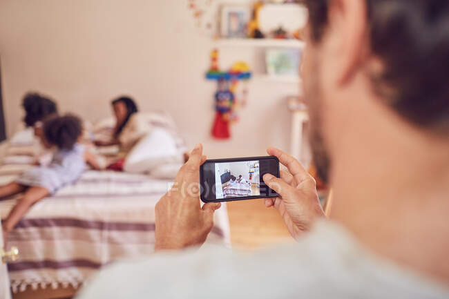 Père avec appareil photo téléphone photographier famille sur le lit — Photo de stock