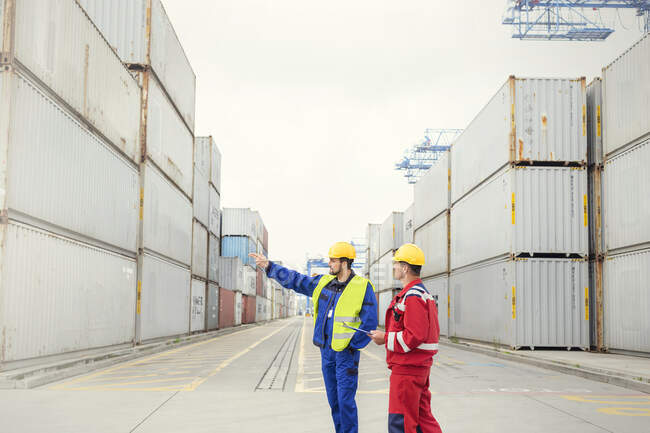 Trabajadores portuarios hablando entre contenedores de carga en el astillero - foto de stock