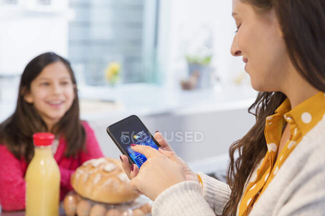 Tochter beobachtet Mutter mit Smartphone in Küche — Stockfoto