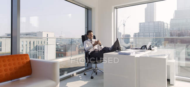Homme d'affaires avec les pieds sur le bureau dans un bureau urbain ensoleillé et moderne — Photo de stock