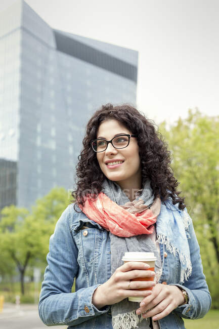 Усміхнена жінка п'є каву в міському парку — стокове фото