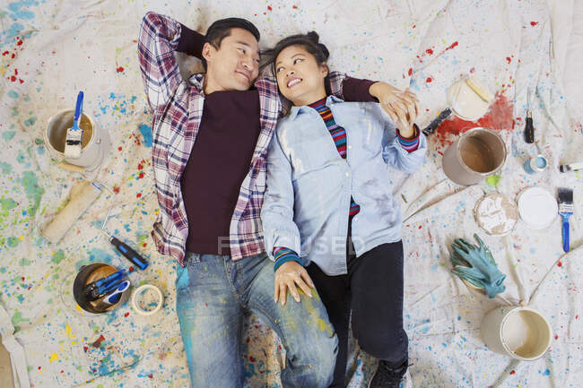 Casal feliz relaxante, fazendo uma pausa da pintura, deitado em pano de gota entre latas de tinta — Fotografia de Stock
