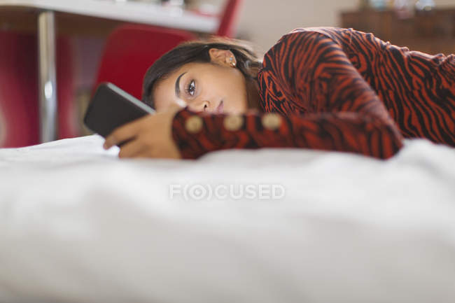 Focalisé adolescent fille à l'aide smartphone pose sur le lit — Photo de stock