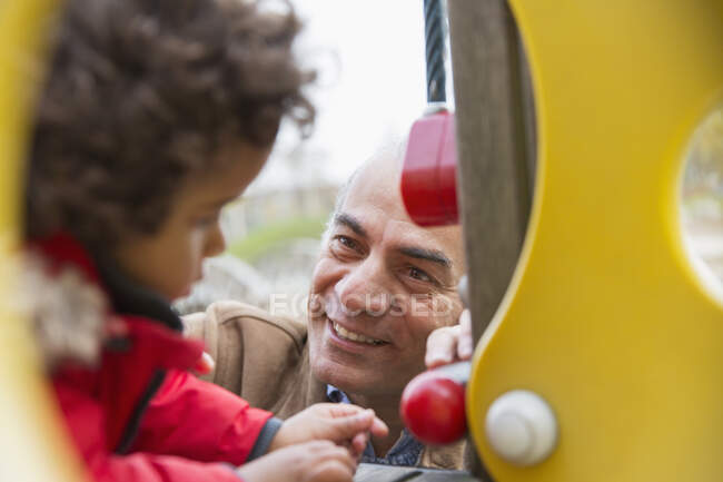 Улыбающийся дедушка играет с внуком на детской площадке — стоковое фото