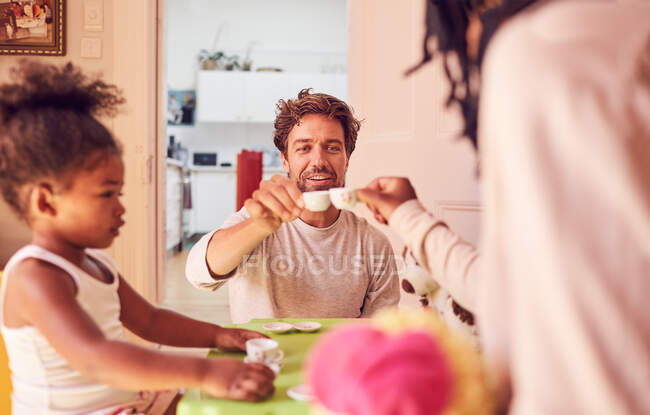 Familia joven disfrutando de una fiesta de té imaginaria - foto de stock